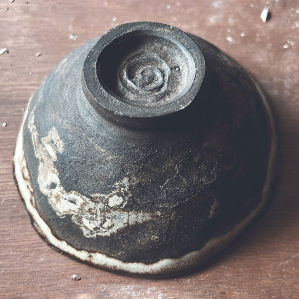 Cuenco de té de cerámica primitiva en negro con el borde claro y el pie en espiral