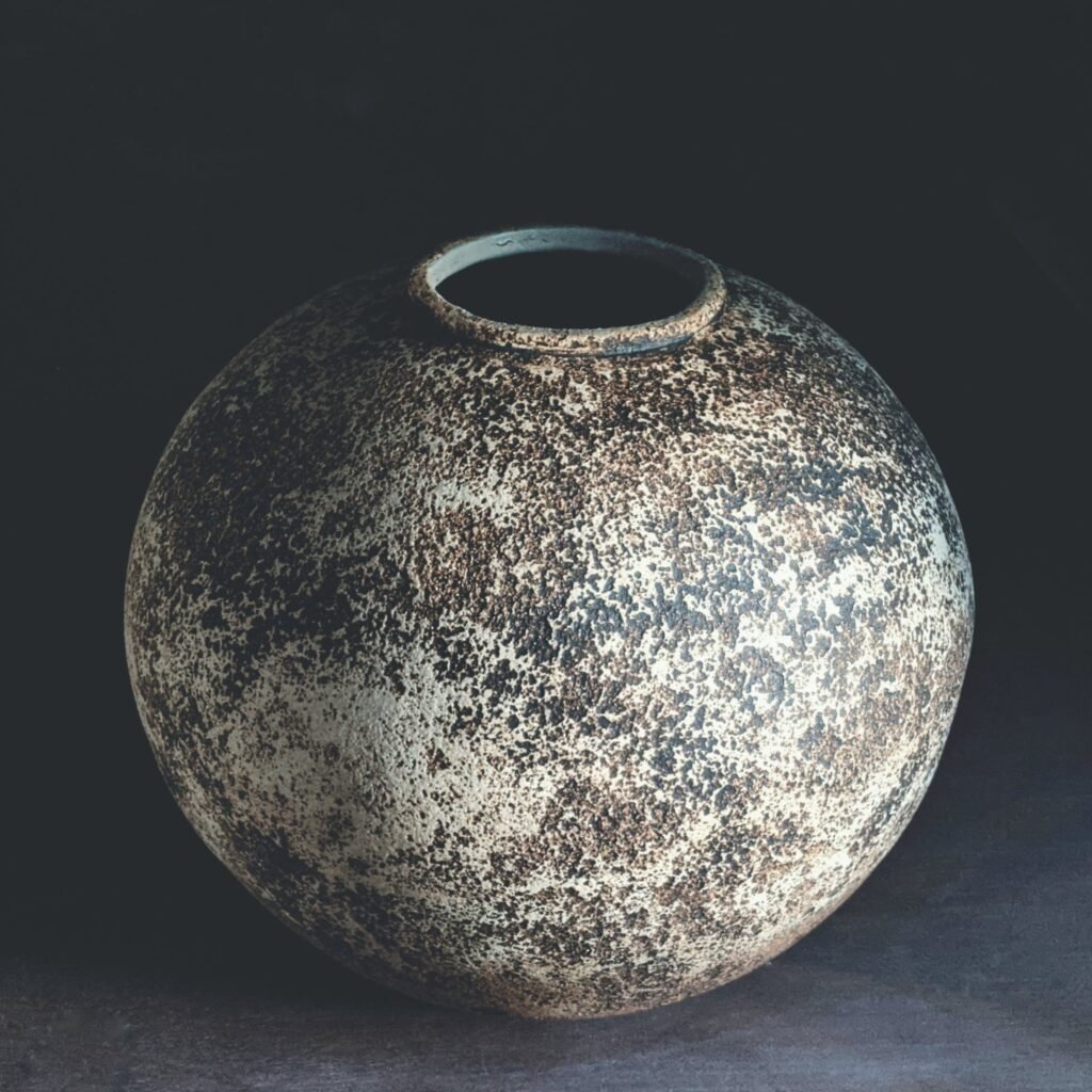 Serie Estratos: vasija esférica de boca ancha con superficie moteada en ocre y negro, como piedra erosionada