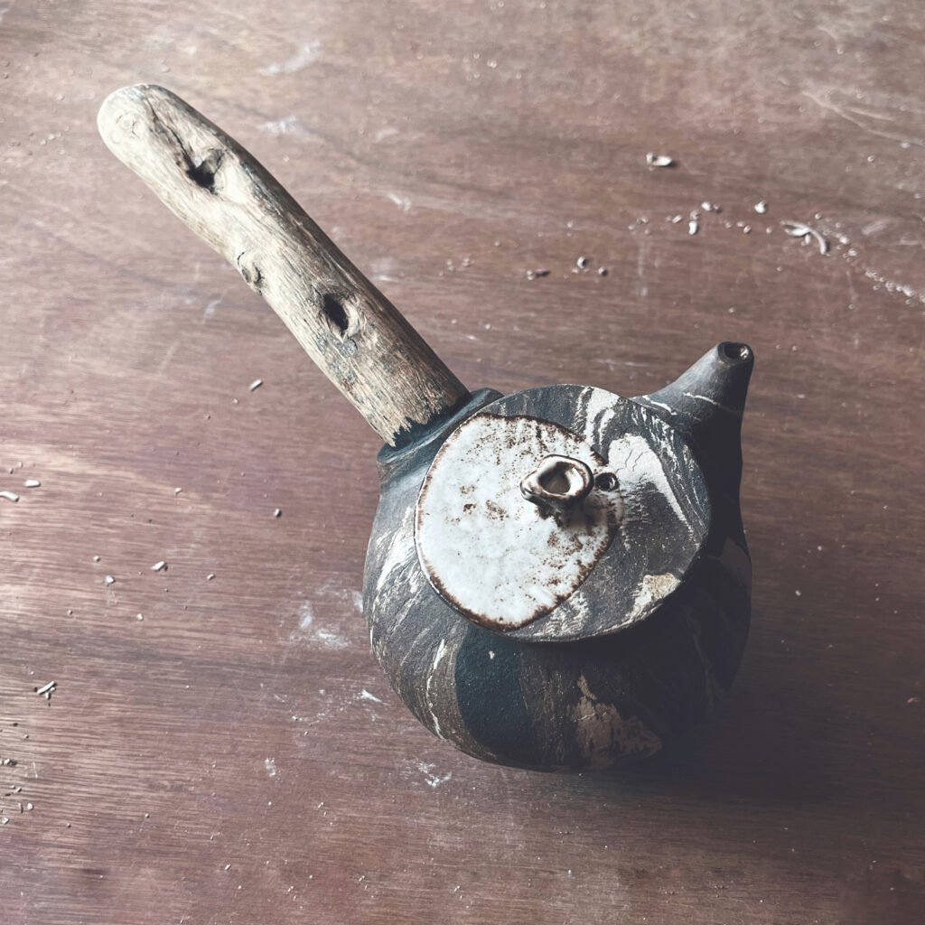 Tetera de cerámica artesanal con asa de rama de madera y cuerpo veteado en blanco y negro