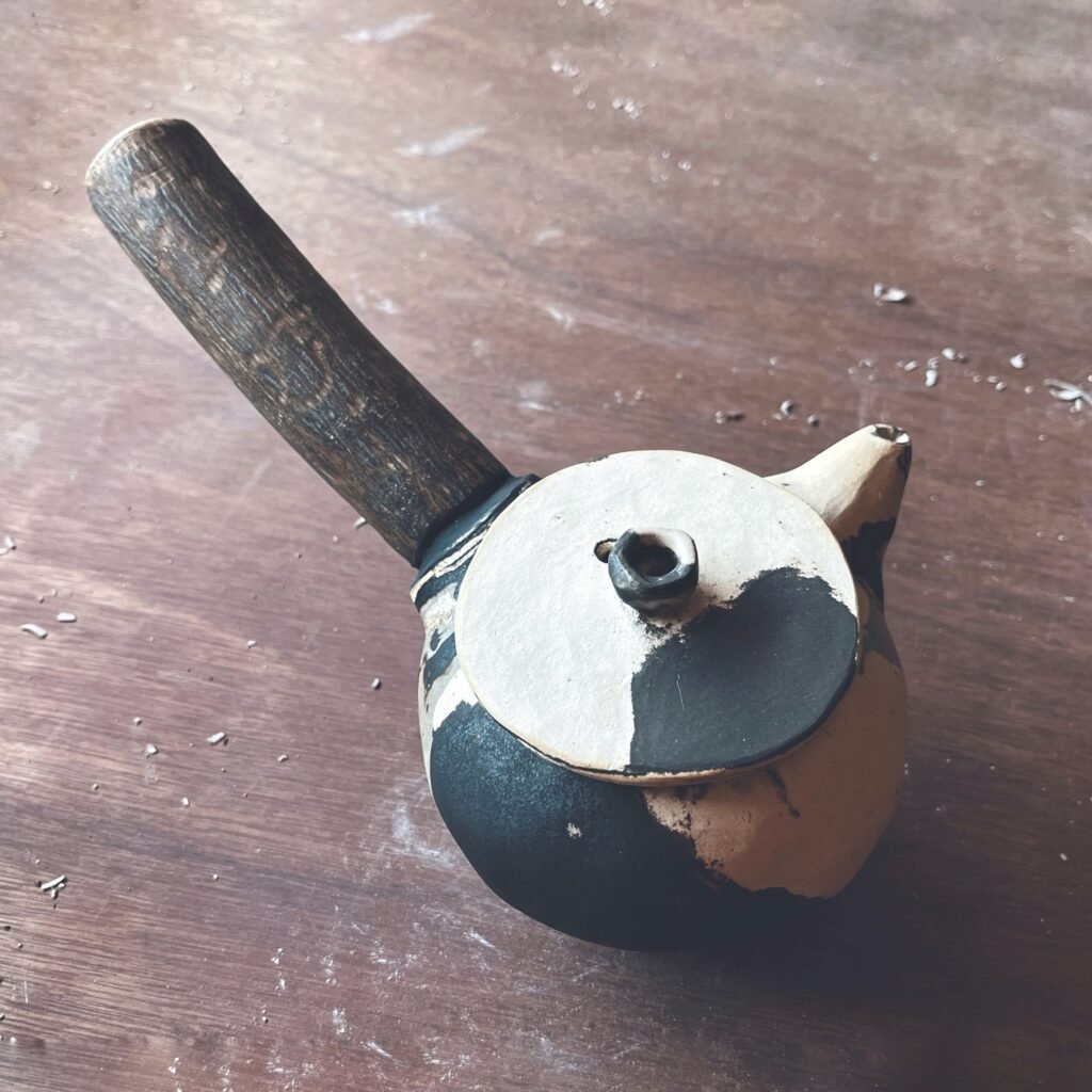 Tetera de cerámica hecha a mano con asa de madera, cuerpo en negro y tapa blanca