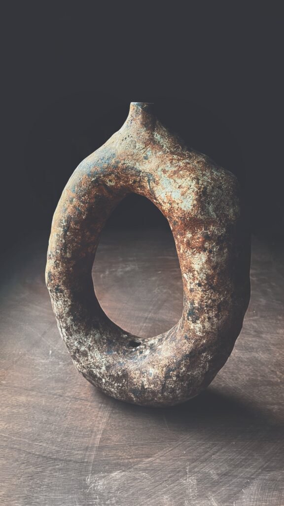 Escultura anular de cerámica primitiva con textura mineral en tonos óxido y verdín
